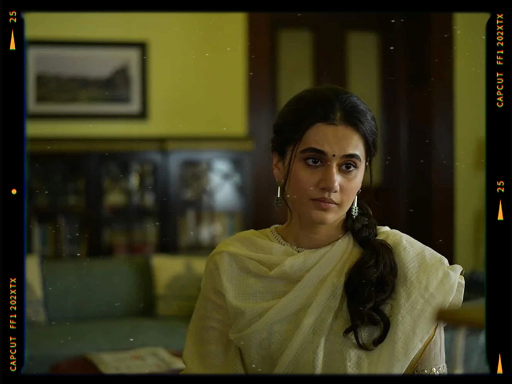A woman with long dark hair styled in a braid, wearing a traditional white saree and jewelry, looking thoughtfully at the camera in a room with a vintage aesthetic.