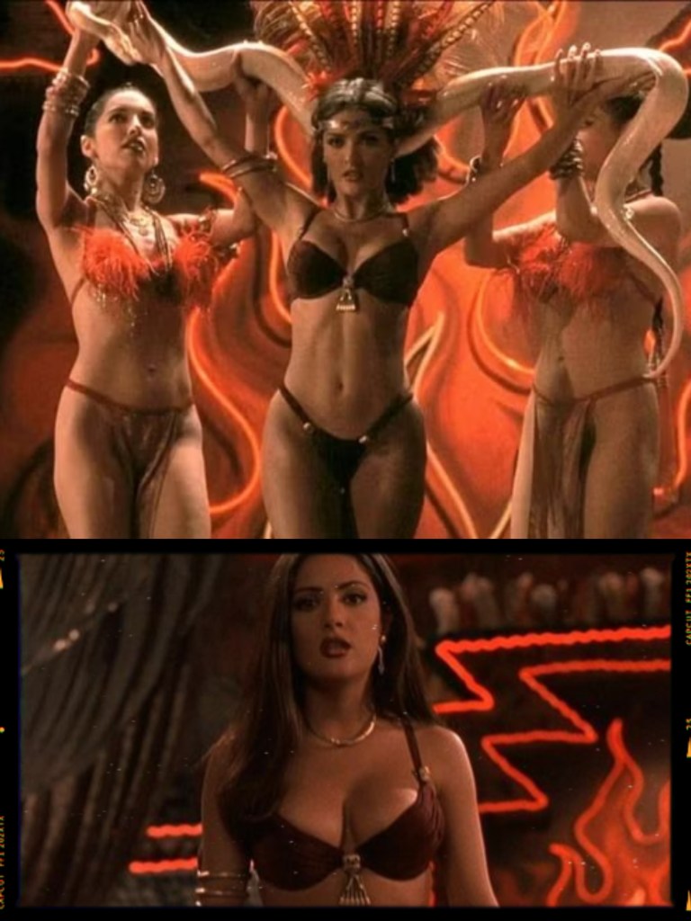 A scene featuring three women in elaborate costumes with feathers and snake accessories, performing in front of a dramatic red background with neon lights.