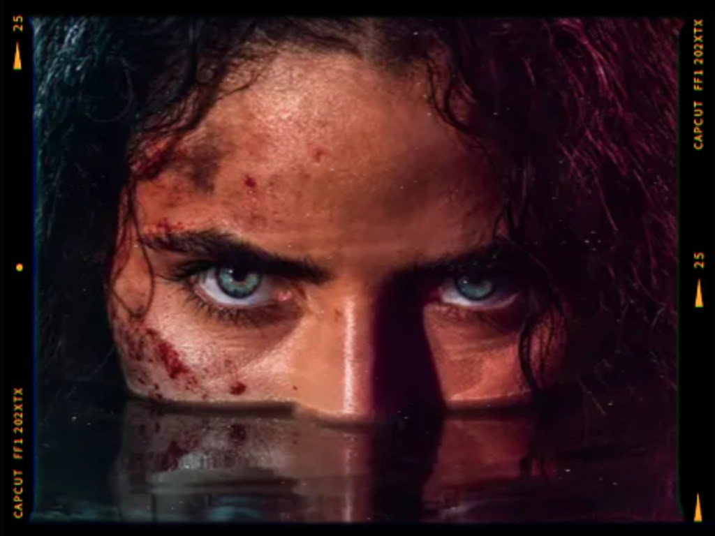 Close-up of a person's face partially submerged in water, with intense blue eyes and visible dirt and scratches on their skin, conveying a dramatic and intense atmosphere.