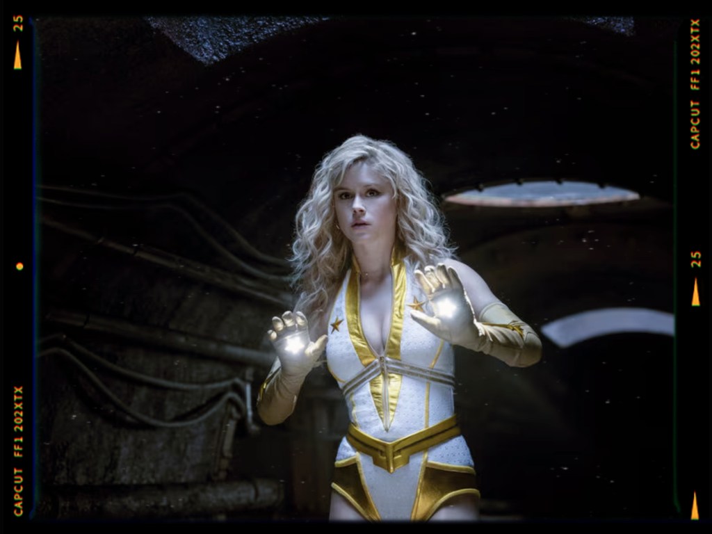 A female superhero wearing a white and gold costume, standing in a dark, industrial setting with glowing lights in her hands.