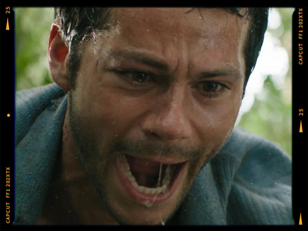 Close-up of a man with a distressed expression, shouting while water drips from his face, set against a blurred green background.