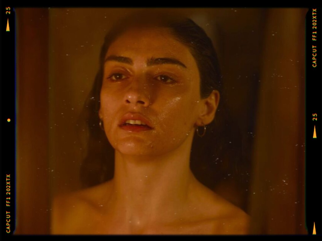 Close-up portrait of a woman with wet skin, staring thoughtfully while standing near a reflective surface.